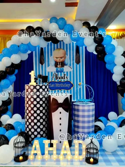 This Boss Baby party decor features a full balloon arch in blue, black, and white over a striped backdrop. Themed plinths and birdcage props add extra detail.