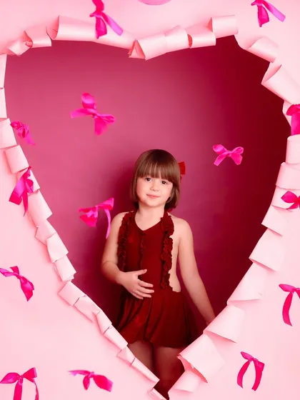 A close-up of the little girl in her red dress, framed perfectly by the heart-shaped cutout. Her gentle expression and the creative framing make this a lovely and artistic portrait.