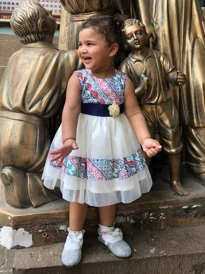 This little one looks so happy in her fusion-style dress. The design features a beautiful printed border on a simple white dress, making it perfect for a festive family function.
