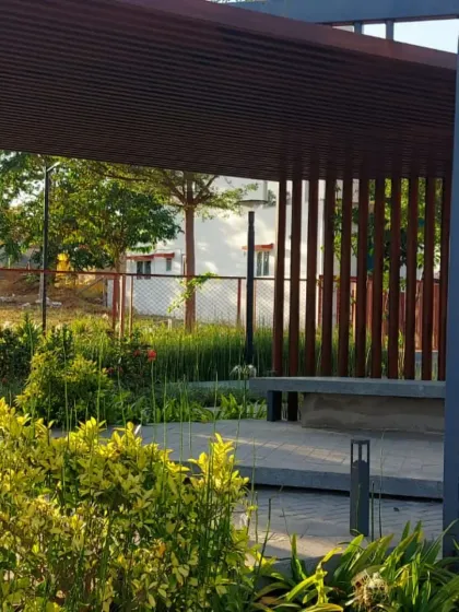 A shaded seating area or bus stop with a modern design, integrated into a park landscape. The surrounding plants soften the structure and provide a pleasant waiting environment.