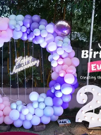A beautiful pastel-themed 25th anniversary decoration for an outdoor event. The balloon ring uses shades of purple, blue, and pink, perfectly complementing the large "25" light-up numbers.