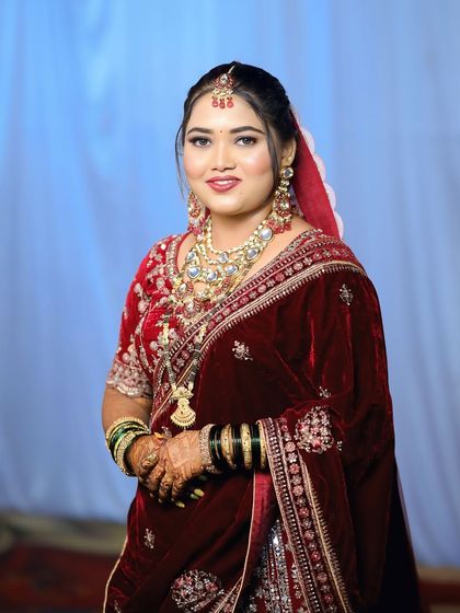 A full view of the bride in her red velvet saree. The complete look, including the hair, makeup, and draping, comes together to create a timeless and elegant bridal appearance.