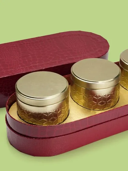 A luxurious red oval box with three golden tins inside. This shot effectively showcases a complete packaging solution for gifting.