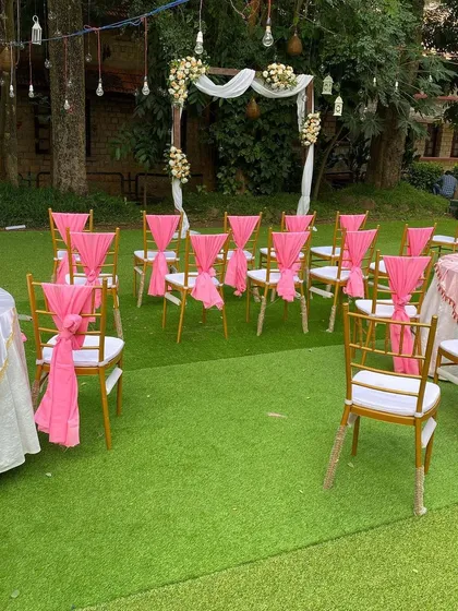 The ceremony space is ready for a beautiful garden wedding. The combination of green lawn, pink accents, and a rustic floral arch creates a picturesque setting.