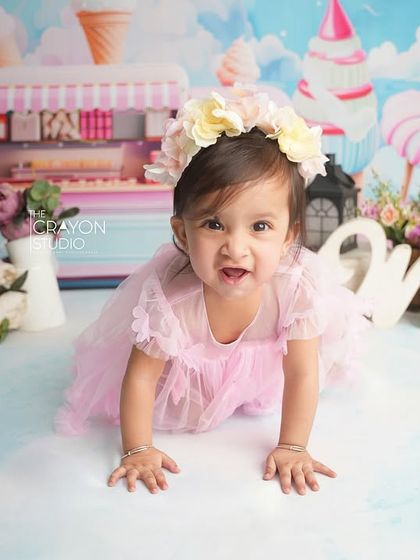 The birthday girl crawls towards the camera with a determined and happy look, showcasing her newfound mobility during her first birthday shoot.