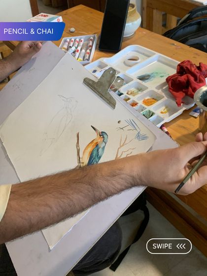 A student begins a watercolor painting of a kingfisher. The initial sketch and light color washes are the first steps in building a detailed and vibrant piece.