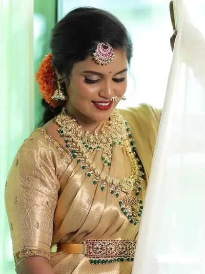 A beautiful bride in a golden saree, wearing a stunning Kempu jewellery set with green bead drops. This is a classic choice for a South Indian Muhurtham.