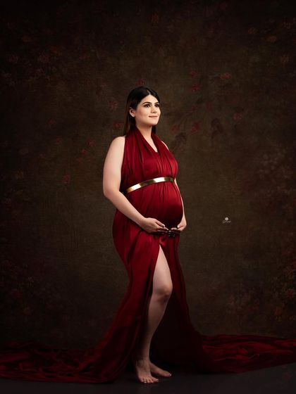 A classic fine art portrait against a dark, textured backdrop. The rich red satin gown and the client's gentle pose create a timeless and sophisticated image.