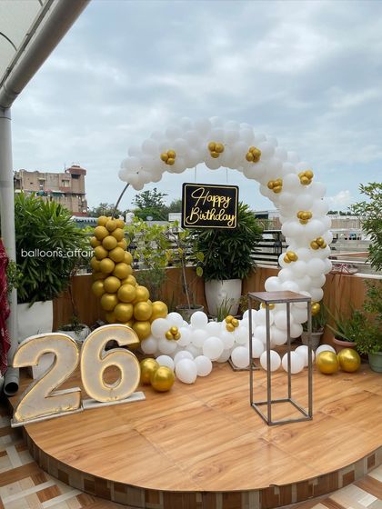 A wide view of the elegant 26th birthday terrace decoration, showing the full semi-circular balloon arch in white and gold.