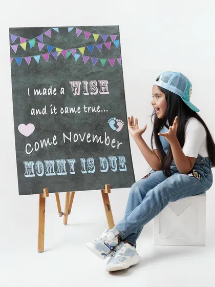 A creative pregnancy announcement photo where a proud big sister-to-be sits next to a chalkboard that reads "I made a wish and it came true... Come November Mommy is due".