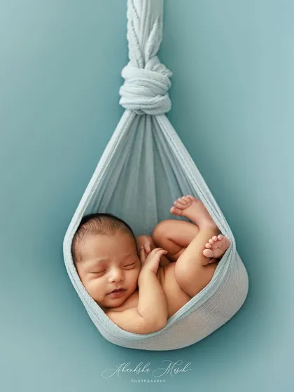 A duplicate image, the hanging sling pose against a simple blue backdrop is a beautiful way to showcase a newborn's tiny, delicate form.