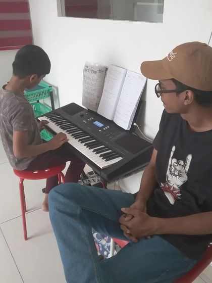 An instructor watches over his student during a keyboard lesson, providing encouragement and feedback.