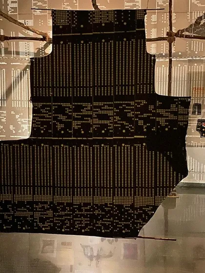 A large textile piece resembling a punch card hangs in the center of the installation.