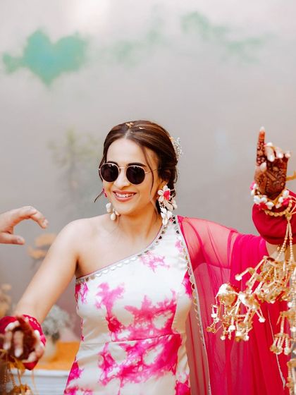 The bride is ready to dance at her Haldi ceremony. Her fun, floral braid is the perfect hairstyle for the occasion, keeping her hair stylishly out of the way.