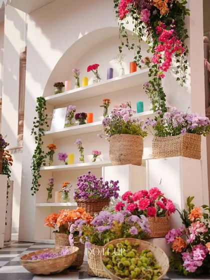 A beautifully styled decor element for the Jaipur Haldi. A white arched shelving unit serves as a vibrant flower market display, filled with colorful blooms in wicker baskets and colorful candles.