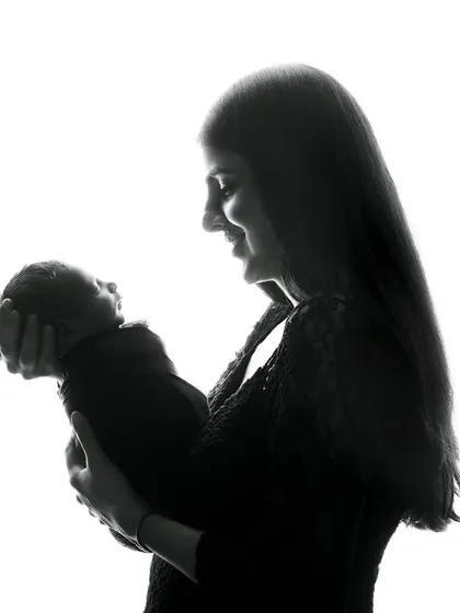 A beautiful silhouette of a mother holding her newborn. This artistic technique uses backlighting to create a dramatic and timeless image that focuses on the iconic shape of the mother and child bond.
