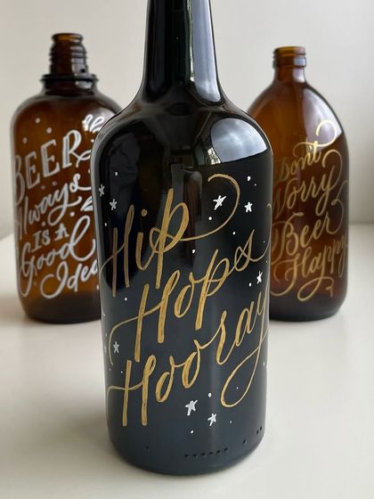 "Hip Hops Hooray." A black bottle with gold and white lettering, adding a touch of fun and festivity to the collection of hand-lettered decor.