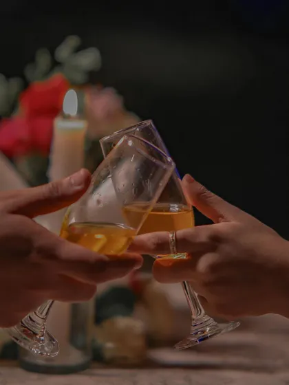 A classic pre-wedding detail shot of a couple making a toast with wine glasses by candlelight. This image captures the intimate and celebratory mood of a romantic evening together.
