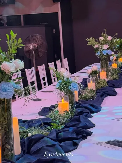 This classic blue and white dining setup is perfect for a refined celebration. We used tall glass vases with blue and white floral arrangements, a deep blue table runner, and pillar candles to create a crisp and elegant look.
