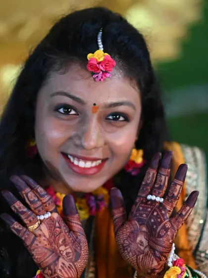 A happy bride on her haldi day, showing off her beautiful mehndi. The dark stain provides a stunning contrast to her yellow attire.