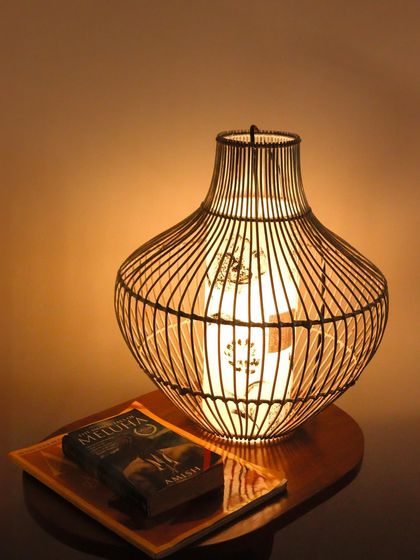 This elegant table lamp features a delicate bamboo cage design. The inner shade casts a soft, patterned light, creating a cozy and sophisticated atmosphere perfect for a reading nook.