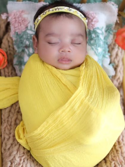 Draped in a flowing yellow wrap, this baby looks like a tiny model. The arrangement of flowers around her adds a touch of sunshine to this beautiful portrait.