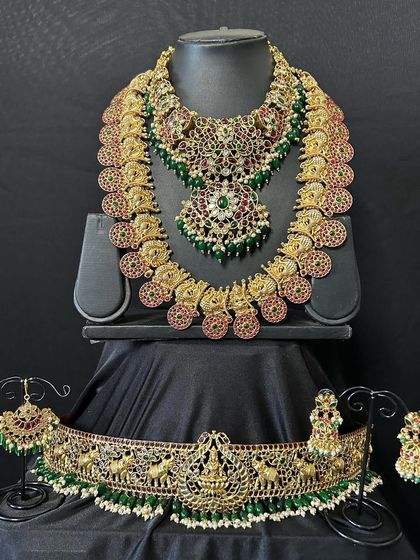 A full view of one of our heaviest bridal sets. This rental includes a choker, a kasulaperu necklace, and a matching vaddanam, all with beautiful detailing and a mix of red and green stones.