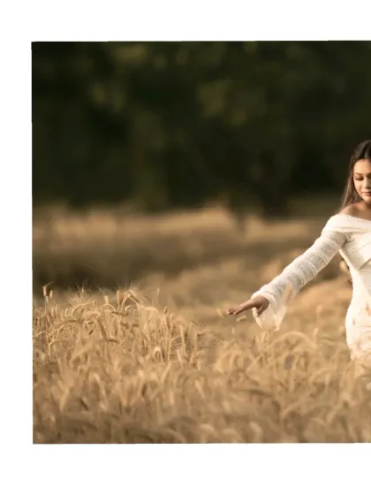 A cinematic shot of the mother-to-be walking through a golden wheat field, her hand gently brushing against the stalks. This image is full of movement and emotion.