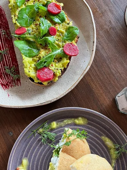 A beautifully plated avocado toast with pickled radish. The artistic smear of beet puree on the plate adds a touch of gourmet flair, elevating a simple cafe dish.