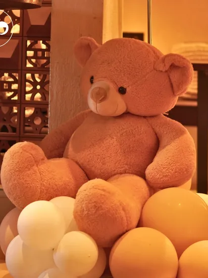 A cuddly teddy bear sits atop a cascade of warm, mustard colored balloons. This simple yet charming detail from our boho themed shower adds a touch of softness and whimsy to the rustic decor.