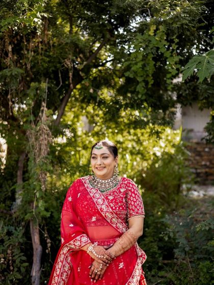 This bride is surrounded by nature, her red lehenga standing out beautifully. The makeup is designed to look fresh and radiant even in bright, outdoor lighting.