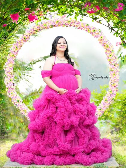 A joyful solo portrait in a vibrant pink ruffled gown, framed by a circular floral prop.