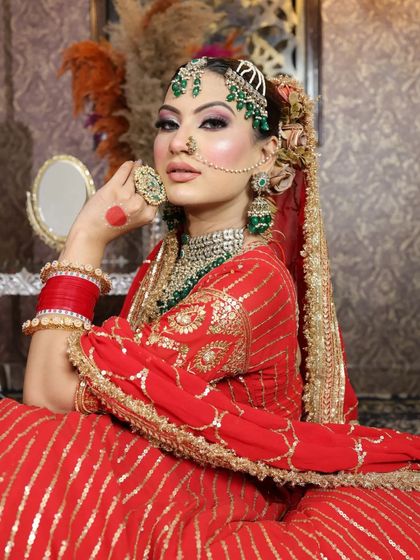 A stunning bridal look in a red georgette lehenga with gota patti work, paired with heavy green stone jewelry.