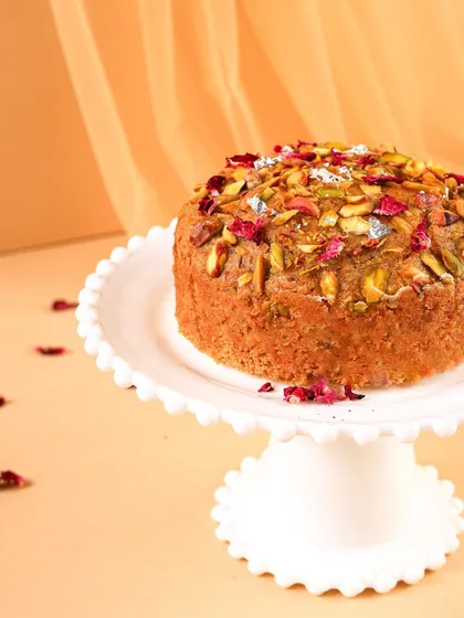 A close-up shot of the Mawa cake, focusing on the rich texture and the beautiful garnish of nuts and petals. This detail shot is all about making you crave a bite.