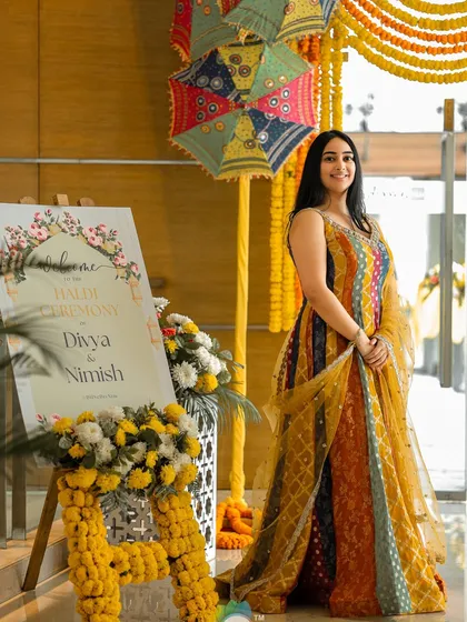 The bride poses by her personalized Haldi welcome sign, which is beautifully decorated with marigolds.