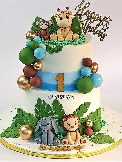 A cute two-tier jungle-themed cake for a first birthday. This design features adorable, cartoonish fondant animals like a giraffe, monkey, elephant, and lion.