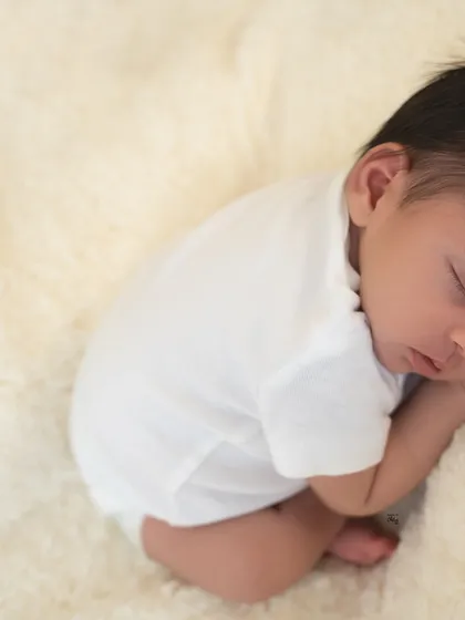 A close-up of the baby in a simple white onesie, curled up and sleeping. This minimalist style is perfect for capturing their natural, tiny form.