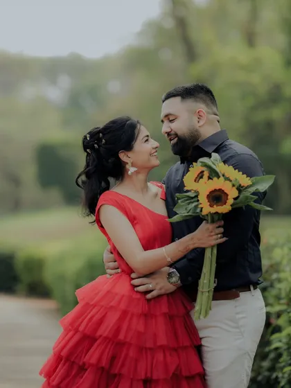 A beautiful pose during a pre-wedding session in a Pune garden. The woman's vibrant red dress stands out against the green foliage, creating a visually stunning and romantic photograph.