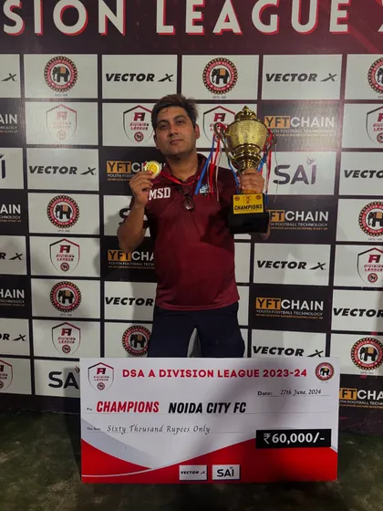 Our director holding the medal and trophy alongside the winner's cheque for the DSA A Division League 2023-24. We don't just play, we win.