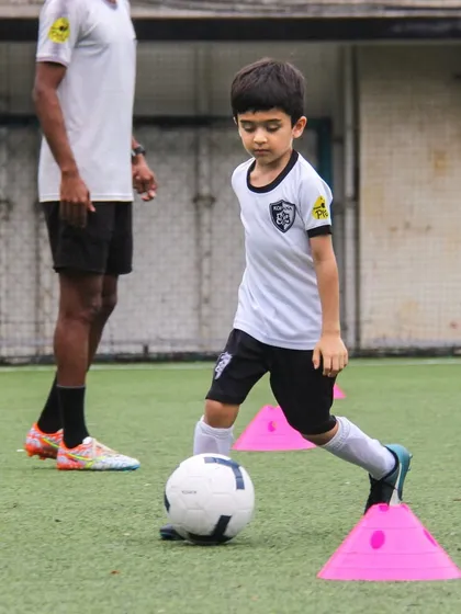 Under the watchful eye of a coach, a player weaves through cones. This drill is essential for improving agility and maintaining control of the ball while changing direction.