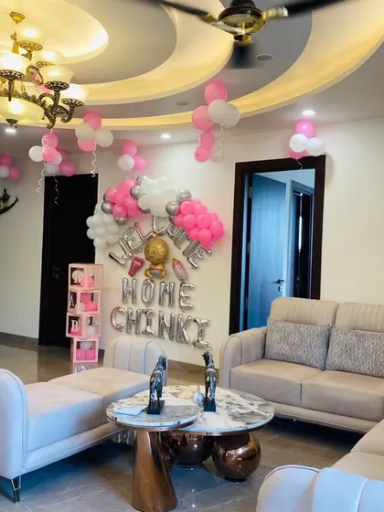 A wide view of a spacious living room decorated for a baby's arrival. The "Welcome Home" balloon setup serves as a beautiful backdrop, with balloons on the ceiling adding to the festive feel.
