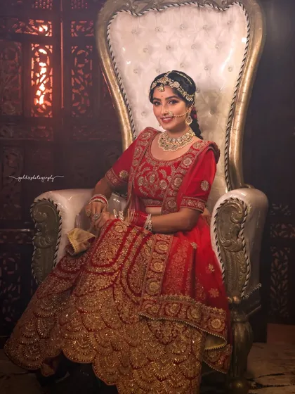 A full-length portrait showcasing a grand bridal lehenga. The bride is seated on a throne-like chair, emphasizing the royal theme of the shoot.