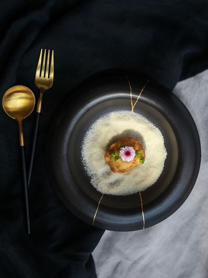 A stunning black plate from the 'Celebrations' collection, styled with a gourmet dish, showcasing its fine dining aesthetic.