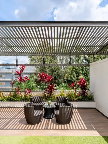 This terrace is all about balanced design. The metal slat pergola creates a beautiful play of light and shadow, providing just enough shade without closing off the sky. A backdrop of vibrant shrubs and a multi-purpose ledge for a pantry or bar make this a highly functional and inviting outdoor living space.