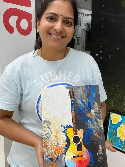 A participant proudly holds up her colorful guitar painting created with a palette knife. The texture adds a dynamic and energetic feel to the piece.