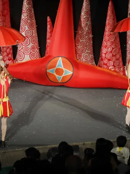 Performers with red umbrellas dance in a shower of confetti, creating a beautiful and celebratory moment in the 'Air Giants Circus'.