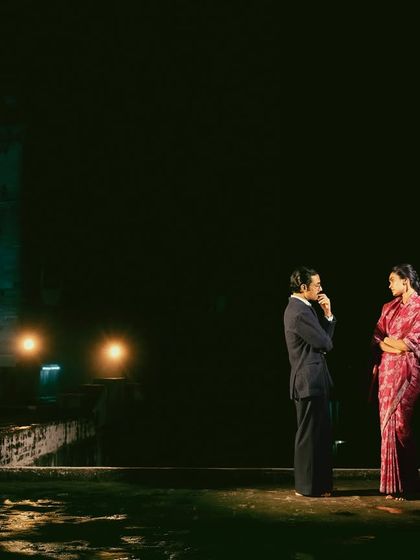 Using negative space to create drama, this shot from the 'Banaras Nocturne' series places the couple in a vast, dark expanse, emphasizing their isolation and the intimacy of their conversation.