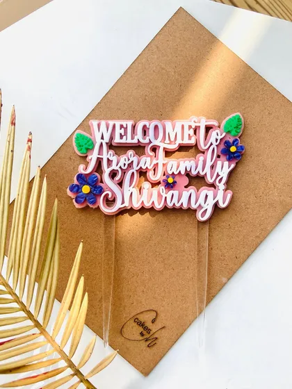 A styled shot of the "Welcome to Arora Family" topper, with a golden palm leaf accentuating its festive feel.