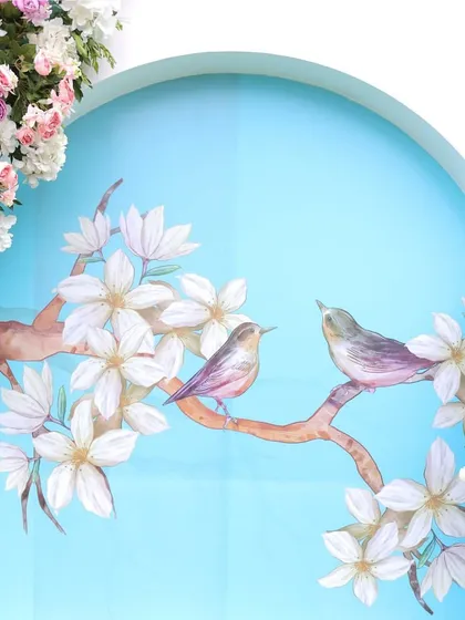 A beautiful detail from the carnival decor, featuring a painted panel with two birds on a branch, framed by soft pink and white flowers.