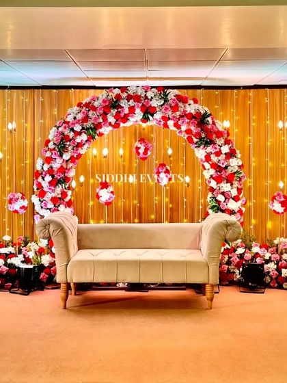 This reception stage is pure enchantment, with a full floral arch of red and white roses set against a backdrop of warm fairy lights, creating a sparkling, romantic setting.